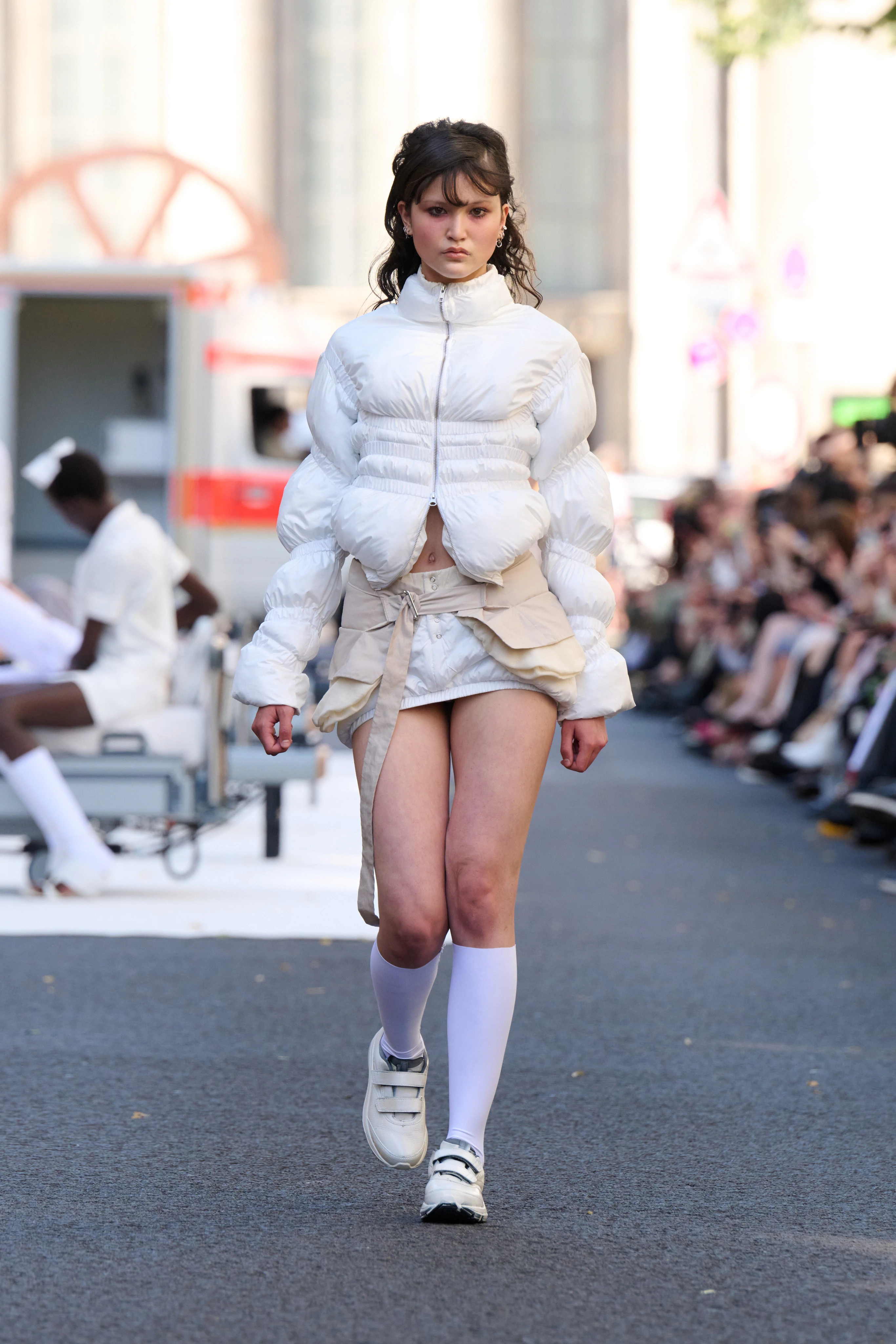 White puffy jacket and skirt from Clara Colette Miramon SS26 collection at Berlin Fashion Week worn by a model. Styled with knee-high socks and flats.