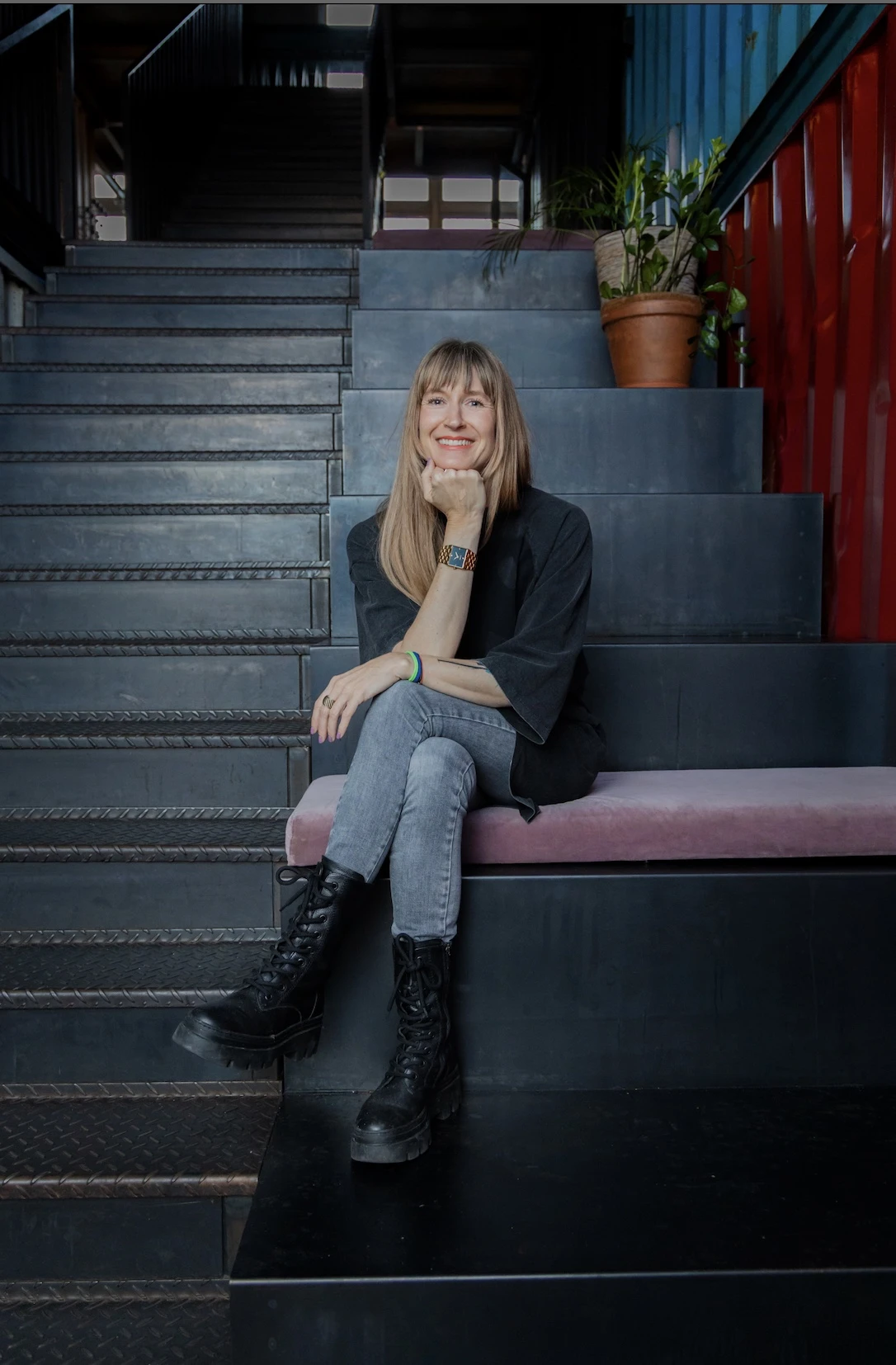Elke Mayer, Festival Director of Zurich Music Week, smiling while seated on a dark metal staircase surrounded by plants.