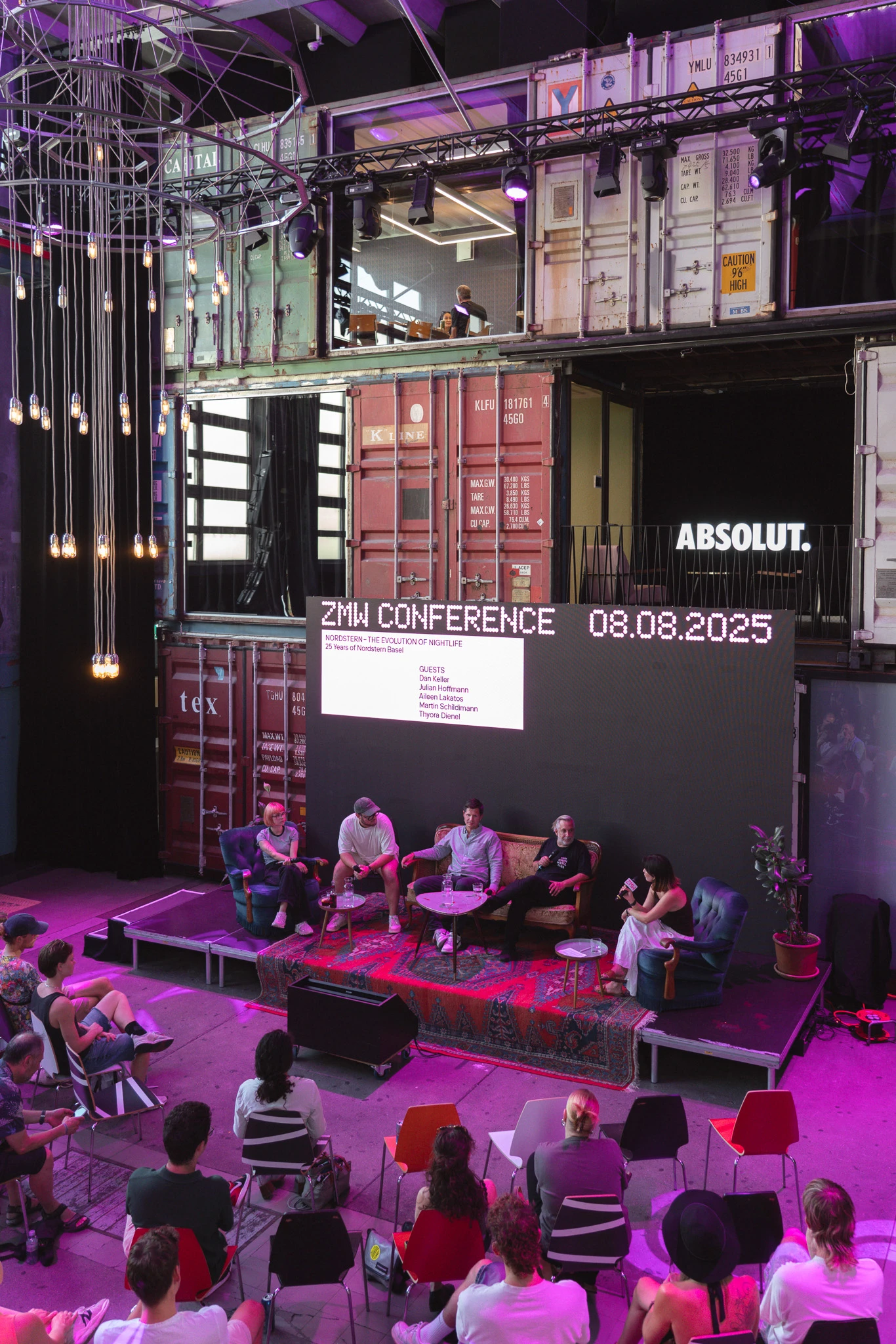 Audience members watching a panel discussion at the Zurich Music Week Conference 2025, staged among shipping containers under purple lighting.